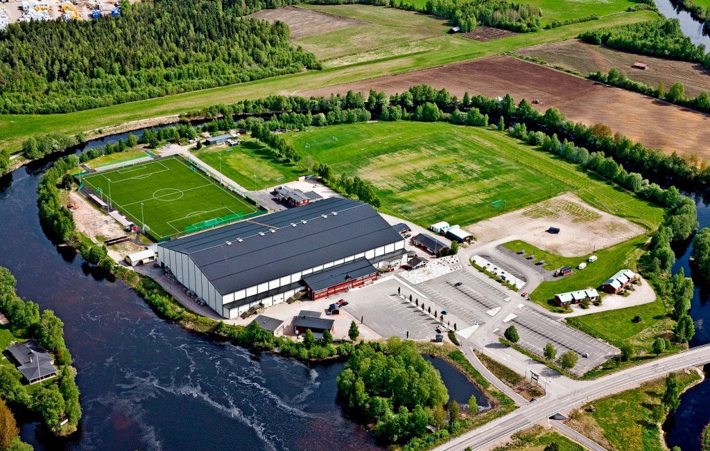 Flygbild över arenan på Ön, omgiven av Voxnan, med fotbollsplaner och parkering